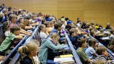 Viele Kinder sitzen in den Reihen eines Hörsaals und schauen nach vorne.