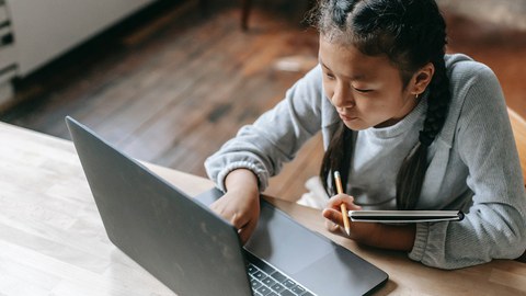 Ein Mädchen sitzt vor einem Laptop.