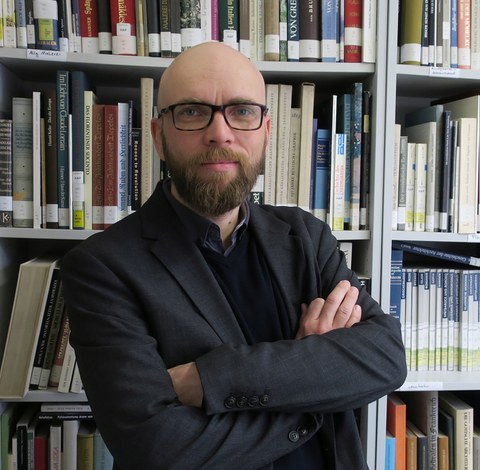 Das Foto zeigt Frank Schmidt, den Moderatoren der Kinder-Uni, vor einem Bücherregal.