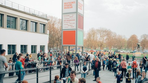 Das Foto zeigt den Vorplatz vom Hygiene-Museum, auf dem viele Kinder und Erwachsene auf den Beginn der Kinder-Uni warten. 