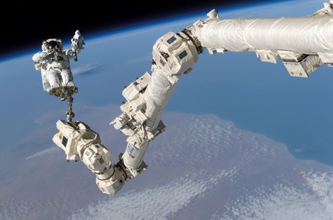 Ein Astronaut bei einem Weltraumspaziergang. Im Hintergrund sieht man einen Teil der Erde von oben.