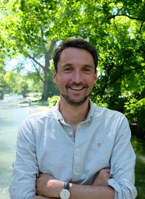 Das Foto zeigt einen Mann in Oberhemd, der freundlich in die Kamera lächelt und vor einem Baum steht.