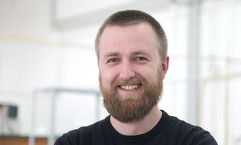 Das Portraitfoto zeigt einen Mann mit kurzem hellbraunen Haar und Vollbart, der freundlich in die Kamera lächerlt.