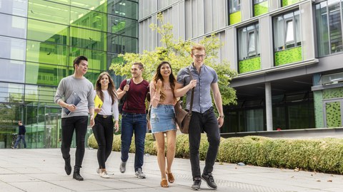 Foto von fünf Studenten, die den Andreas-Pfitzmann-Bau verlassen und sich dabei unterhalten.