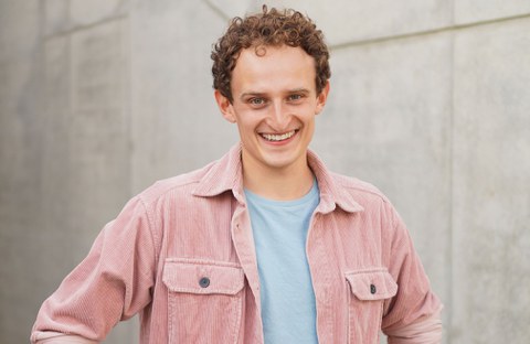 Julian Janssen steht vor einer Wand und lacht in die Kamera.