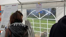 Das Foto zeigt 3 Personen, die sich mit einer Kugelbahn beschäftigen. Die Kugelbahn steht in der Mitte des Bildes auf einem Tisch in einem Festzelt.