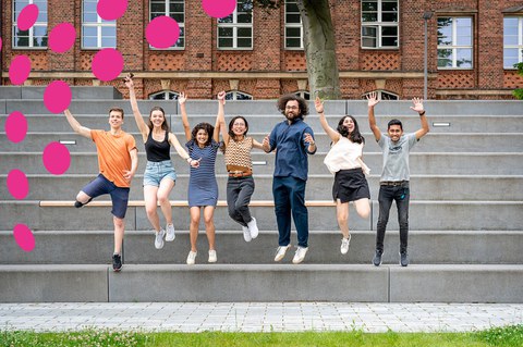 Bild zeigt 7 Studierende, die mit erhobenen Armen lachend von einer Treppe am Fritz-Foerster-Bau springen.