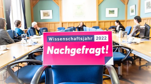 Logo des Wissenschaftsjahres vor Stuhl im Hintergrund Menschen