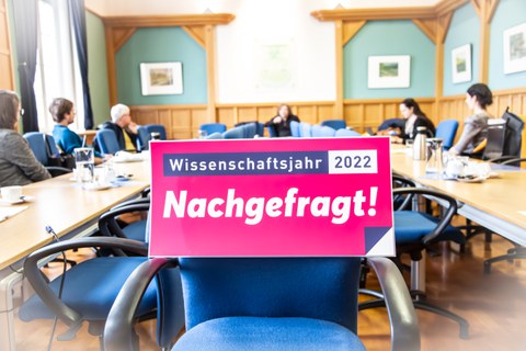 Logo des Wissenschaftsjahres vor Stuhl im Hintergrund Menschen