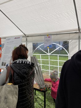 Das Foto zeigt 3 Personen, die sich mit einer Kugelbahn beschäftigen. Die Kugelbahn steht in der Mitte des Bildes auf einem Tisch in einem Festzelt.