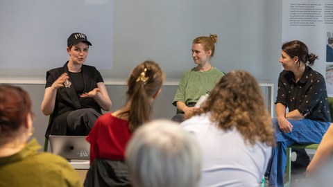 Drei Personen sitzen auf der Bühne und sprechen vor einem Publikum