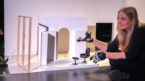 Eine Person sitzt vor einem kleinen Raummodell und trägt Motion Capture Handschuhe.