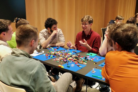 7 Studierende aus Medizin, Informatik und Ingenieurwissenschaften sitzen an einem Tisch und bauen mit LEGO-Steinen an gemeinsamen Projektideen