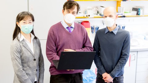 Drei Menschen stehen mit Mund-Nasen-Bedeckung vor einem Rednerpult.
