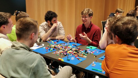 7 Studierende aus Medizin, Informatik und Ingenieurwissenschaften sitzen an einem Tisch und bauen mit LEGO-Steinen an gemeinsamen Projektideen