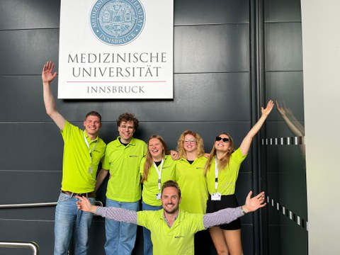 PEC-Team mit MITZ-T-Shirts vor einem Schild Medizinische Fakultät Innsbruck - von links nach rechts: Johannes Achberger, Willi Paul Bläk, Franziska Grosser (Betreuung), Maximilian Winkelkotte, Theresa Pleyer, Annelina Weiß