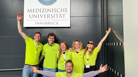 PEC-Team mit MITZ-T-Shirts vor einem Schild Medizinische Fakultät Innsbruck - von links nach rechts: Johannes Achberger, Willi Paul Bläk, Franziska Grosser (Betreuung), Maximilian Winkelkotte, Theresa Pleyer, Annelina Weiß