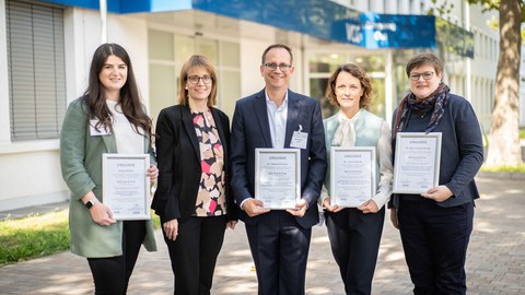 Das Foto zeigt fünf Personen, von denen vier eine Urkunde in der Hand halten.