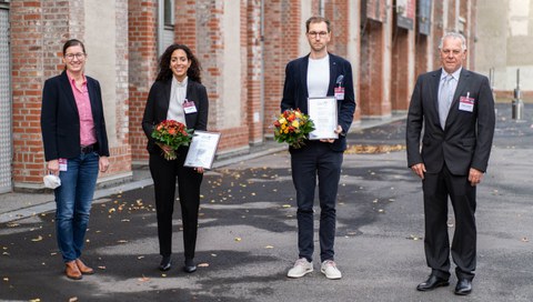 Auf dem Foto sind vier Personen zu sehen, zwei Frauen und zwei Männer. Je eine Frau und ein Mann halten Blumen und eine Urkunde in der Hand.