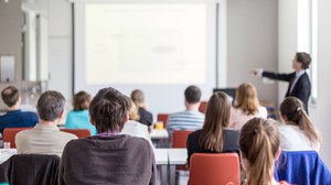 Das Foto zeigt eine Seminargruppe, die dem Vortrag eines Dozenten zuhört.