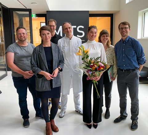 Das Foto zeigt eine Gruppe Personen. Die Frau in der Mitte hält Blumen in der Hand.