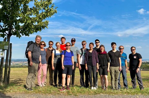 Das Foto zeigt eine Gruppe Menschen, die vor einem Feld stehen und in die Kamera lächeln.