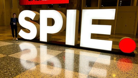 Das Foto zeigt eine junge Frau vor dem Logo der SPIE in San Francisco.