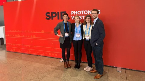 Das Foto zeigt vier Personen vor einer roten Wand mit dem Logo der Photonics West Konferenz.