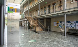 Das Foto zeigt den Eingangsbereich des Medizinisch-Theoretischen Zentrums. Dieses befindet sich im Universitätsklinikum der TU Dresden. Im Vordergrund steht eine große Informationstafel. Auf dieser ist die Lage der einzelnen Räume erkennbar. 