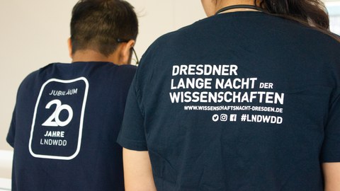 Zwei Personen stehen mit Rücken zu Kamera. Auf dem Rücken des T-Shirts steht Lange Nacht der Wissenschaften 2023