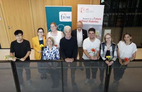 Eine Gruppe lächelnder Wissenschaftlerinnen und Wissenschaftler steht in einer Reihe vor Bannern des DZD und DZNE.
