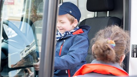 Kind mit Basecap sitzt auf dem Fahrersitz eines Krankenwagens und freut sich.