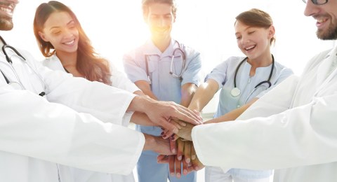 Junge Mediziner:innen stehen im Kreis und legen die Hände aufeinander