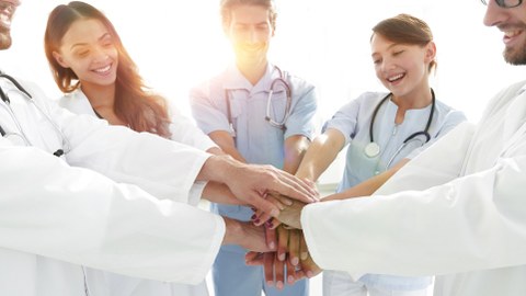 Junge Mediziner:innen stehen im Kreis und legen die Hände aufeinander