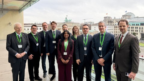 Zehn Personen stehen auf einer Terasse mit dem Ausblick auf das Brandenburger Tor und den Bundestag in Berlin.