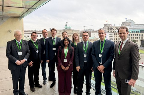 Zehn Personen stehen auf einer Terasse mit dem Ausblick auf das Brandenburger Tor und den Bundestag in Berlin.