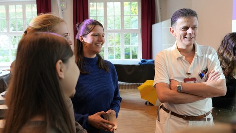 Links im Seminarraum stehen junge Frauen und schauen einen Mann rechts an. Der Mann trägt ein Namensschild mit dem Logo des Klinikums Chemnitz.