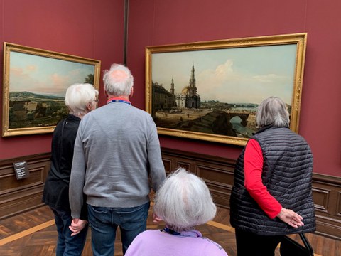 Vier ältere Menschen betrachten in einem Museum eine Stadtansicht Dresdens.