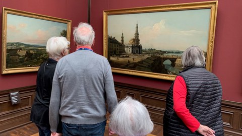 Vier ältere Menschen betrachten in einem Museum eine Stadtansicht Dresdens.