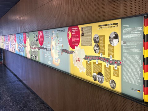 Eine lange, bunte und beleuchtete Infotafel an der Wand.
