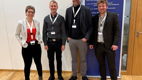 Vier Personen stehen in einer Reihe und lächeln.