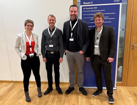 Vier Personen stehen in einer Reihe und lächeln.