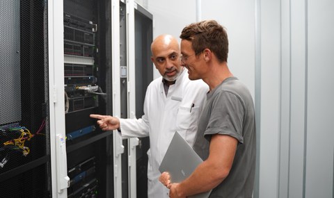 Zwei Männer stehen vor einem Switchboard und unterhalten sich darüber.