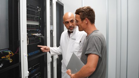 Zwei Männer stehen vor einem Switchboard und unterhalten sich darüber.