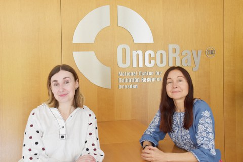 Zwei Frauen sitzen am Tisch. Im Hintergrund Text an der Wand: OncoRay - National Center for Radiation Research Dresden.