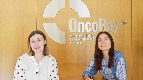 Zwei Frauen sitzen am Tisch. Im Hintergrund Text an der Wand: OncoRay - National Center for Radiation Research Dresden.