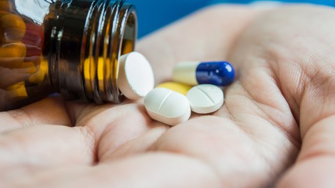 Eine Frauenhand schüttelt Tabletten aus einem Behältnis.