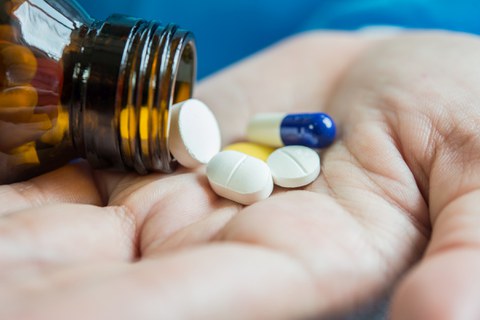 Eine Frauenhand schüttelt Tabletten aus einem Behältnis.