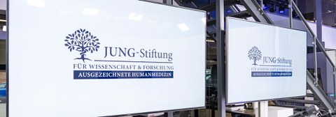 Gespiegelte weiße Tafel mit blauem Text darauf: Jung-Stiftung für Wissenschaft und Forschung, Ausgezeichnete Humanmedizin