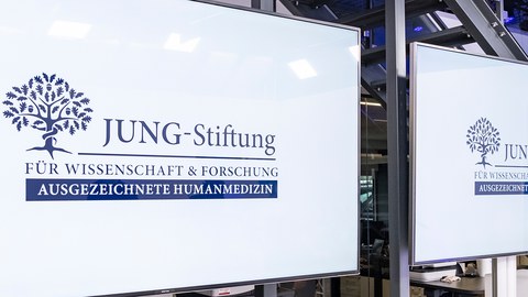 Gespiegelte weiße Tafel mit blauem Text darauf: Jung-Stiftung für Wissenschaft und Forschung, Ausgezeichnete Humanmedizin